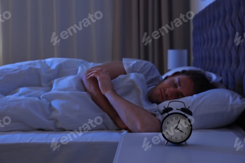 Preview: Alarm clock on nightstand near sleeping young man. Bedtime