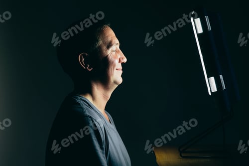 Preview: Smiling middle aged man sitting in front of a light therapy box.