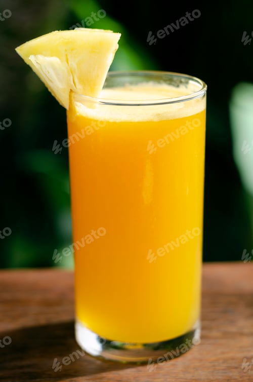 Preview: glass of fresh organic pineapple juice on table outdoors