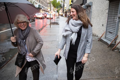 Preview: Two women walking together under umbrella on rainy day in city