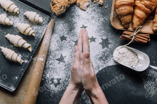 Preview: cropped image of woman rubbing flour between hand palms over table with dough for croissants on tray