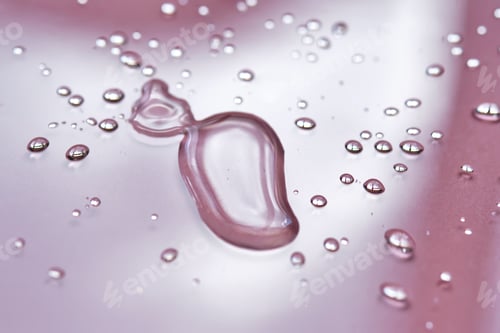 Preview: A large drop and splashes of micellar water on a pink background.