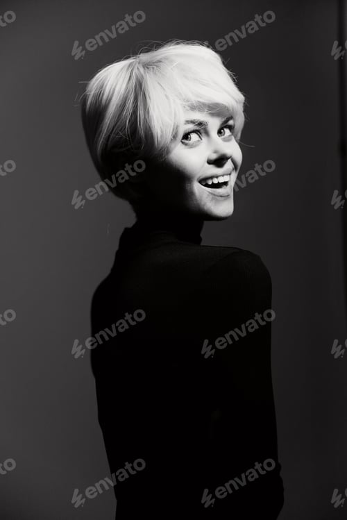 Preview: Smiling woman with short blonde hair in a black turtleneck, against a monochrome backdrop, exuding