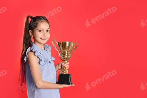 Preview: Happy girl with golden winning cup on red background. Space for text