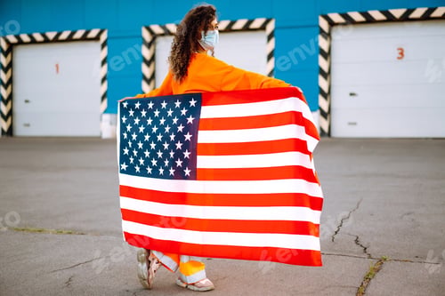 Preview: African American woman with medical face mask posing with american flag. Covid-2019.