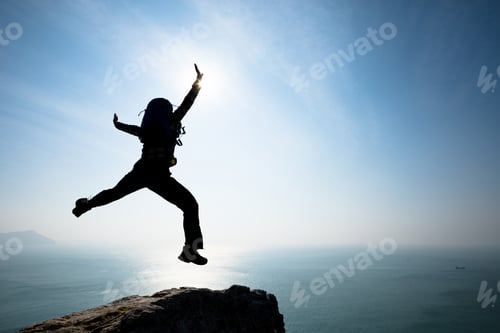 Preview: Hipster backpacker jumping on sunrise seaside cliff edge