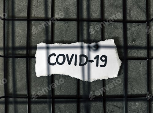 Preview: Overhead, top view of covid-19 text written on piece of paper inside a black cage