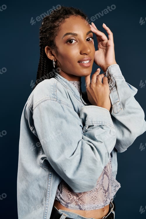 Preview: Young woman in stylish attire poses gracefully against a dark blue backdrop in a chic setting