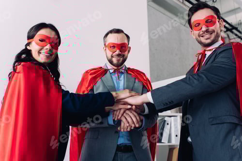 Preview: super businesspeople in masks and capes putting hands together in office