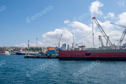Preview: Cargo ships docked at a busy harbor with cranes and a clear blue sky in the background during midday