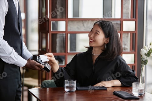 Preview: Smiling young woman paying with credit card in luxury restaurant