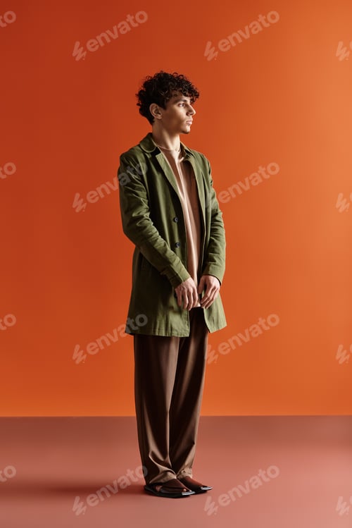 Preview: Stylish young man poses confidently against a vibrant orange backdrop in a modern setting