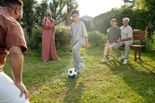 Preview: Teenage Boy Kicking Soccer Ball While Family Watching and Smiling Outdoors