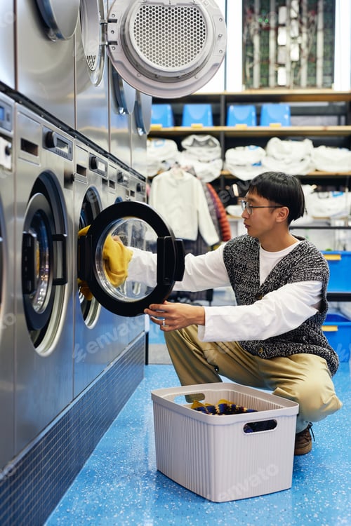 Preview: Asian Man Loading Dirty Clothes into Washing Machine at Coin Laundromat