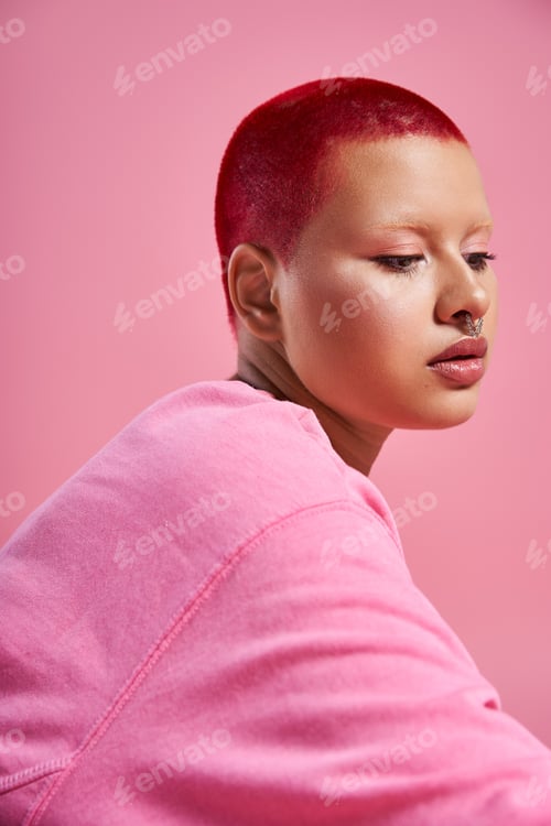 Preview: Young woman with short pink hair and a nose piercing in vibrant fashion in a studio