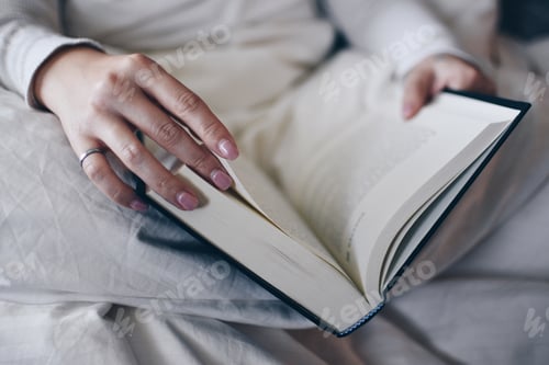 Preview: Girl reading in bed under cozy blankets. Open book