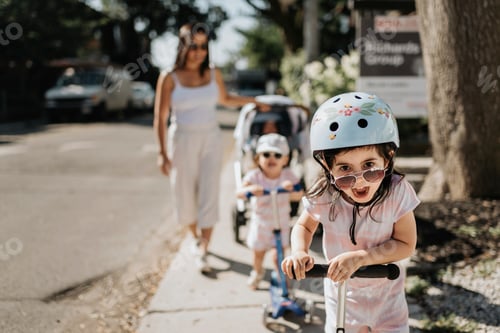 Preview: Excited child in a helmet playfully scooting on a sunny day with family nearby.