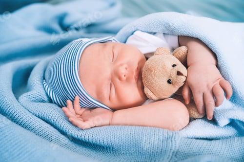 Preview: Portrait of new born baby one week old with cute soft toy in crib in cloth background.