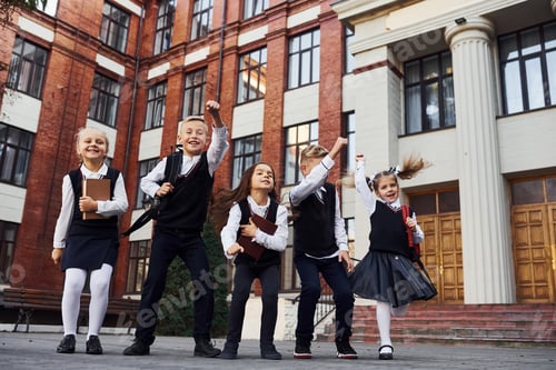 Preview: Group of kids in school uniform jumping and having fun outdoors together near education building