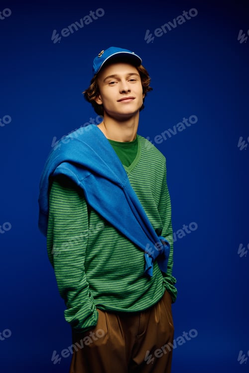 Preview: Stylish young man showcases modern fashion trends in vibrant blue backdrop