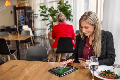 Preview: Businesswoman using digital tablet while talking through earphones at restaurant