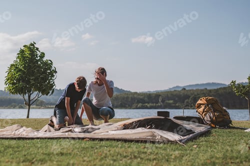 Preview: Family setting up a tent camping on a grassy overlooking the calm lake family enjoys a shared activi