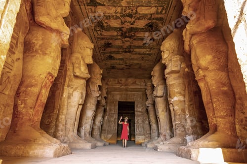 Preview: A young woman in a red dress at the Abu Simbel Temple next to the sculptures