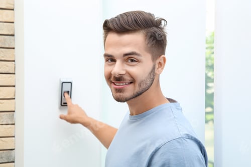 Preview: Young man pressing fingerprint scanner on alarm system indoors