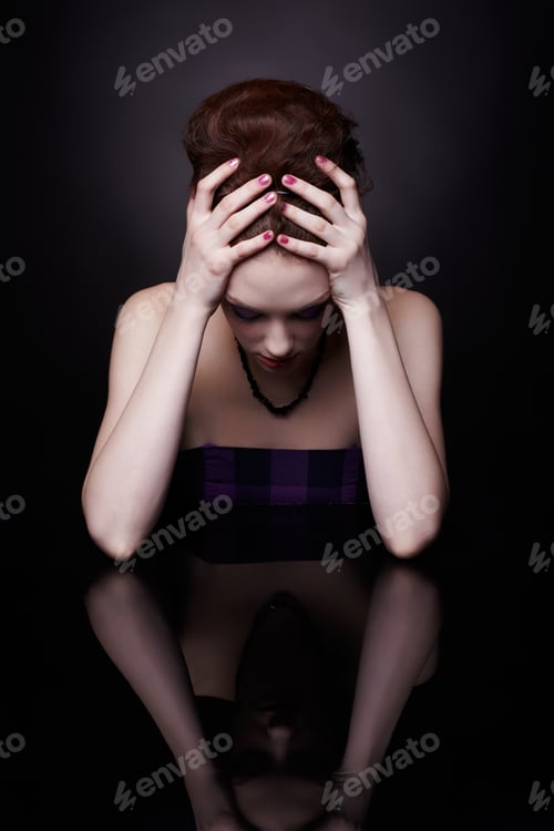Preview: Portrait Of Tired Beautiful Young Woman Sitting At Dark Mirror Surface Holding Her Head With Hands