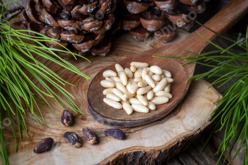 Preview: Pine nuts in the spoon and pine nut cone on the wooden table. Organic food.