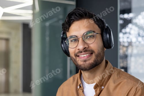 Preview: Close-up portrait of a young Indian man wearing headphones working and studying in the office