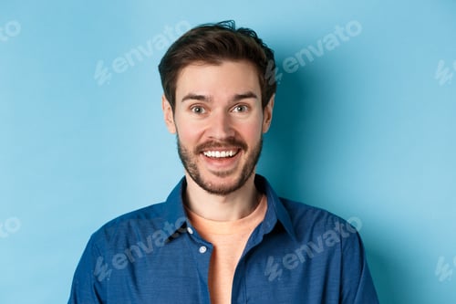 Preview: Close up of surprised handsome guy with beard looking amused, smiling happy at camera, standing on