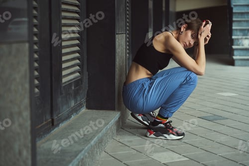 Preview: City woman in sportswear sits near wall of city building