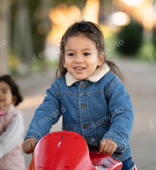 Preview: Portrait of happy latin child driving red toy motorcycle in park