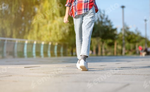 Preview: A girl in a plaid shirt jumps and runs along a path in a city park on a sunny summer day.