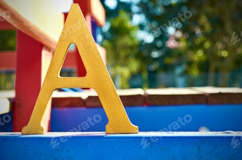 Preview: Closeup of a big yellow uppercase A letter in the park with the trees in the blurred background