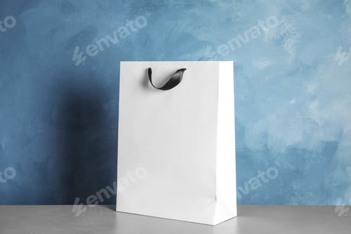 Preview: Paper shopping bag on table against color background. Mock up for design
