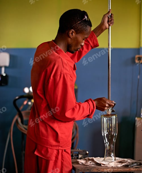 Glassblower Shaping Clear Glass with Tool in Workshop