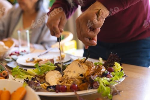 Preview: Hands of biracial senior man cutting meal at christmas dinner in sunny dining room
