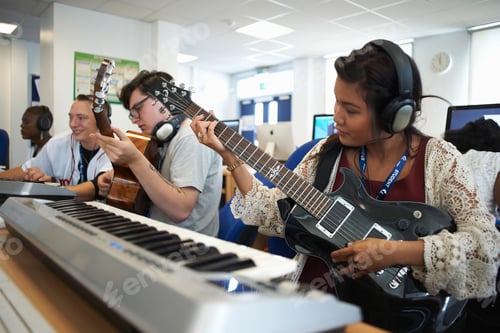 Visualização: Pequeno grupo de estudantes universitários sentados na frente de teclados usando fones de ouvido tocando guitarra