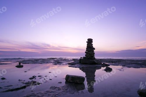 Preview: Beautiful view of a stack of balanced pebbles on the seashore at sunrise