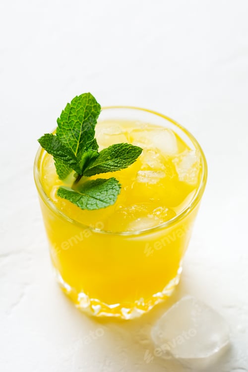 Preview: One Glass of Orange juice with mint leaves and ice on white stone rustic background. Selective focus