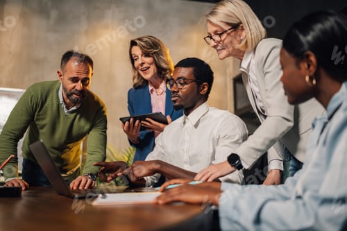 Preview: Interracial chief commenting project on a laptop with his team at office