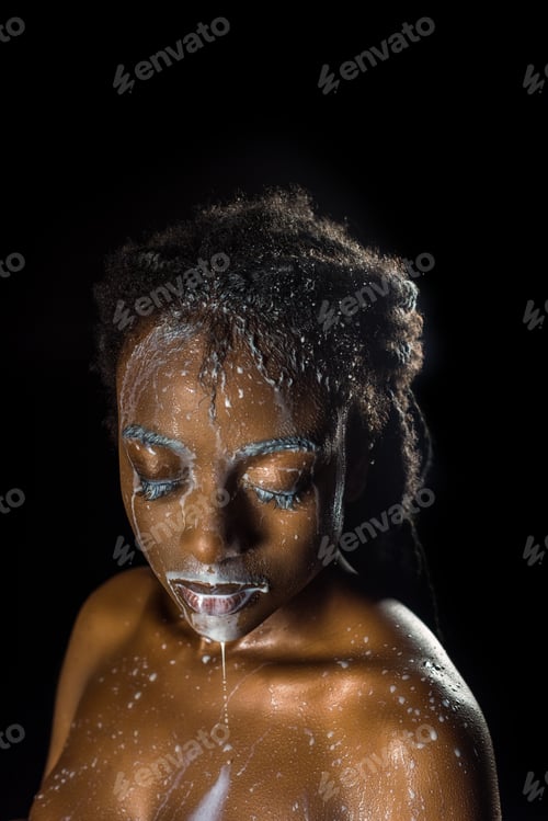 Preview: seductive african american girl with milk drops on face and body posing with closed eyes isolated on