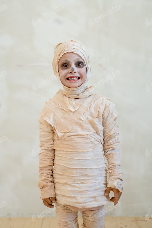 Preview: Cute little boy in mummy costume standing against white wall
