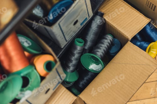 Preview: high angle view of various sewing strings in cardboard boxes at workshop