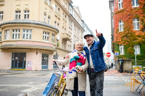 Preview: Happy senior couple with bicycle outdoors on street in city.