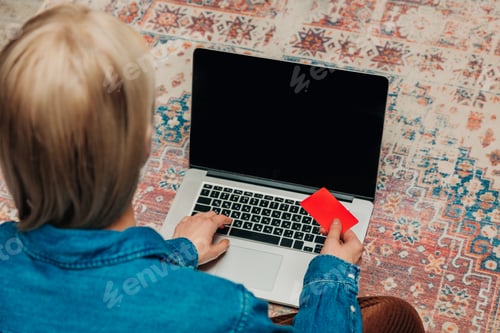 Preview: woman sitting on a carpet with a laptop, completes an online purchase.