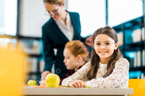 Visualização: linda estudante sorrindo para a câmera enquanto estudava com colega de classe e professor na biblioteca