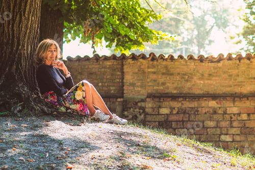 Preview: senior fit happy lady relax sit next to tree in park wear floral skirt and black long sleeve shirt